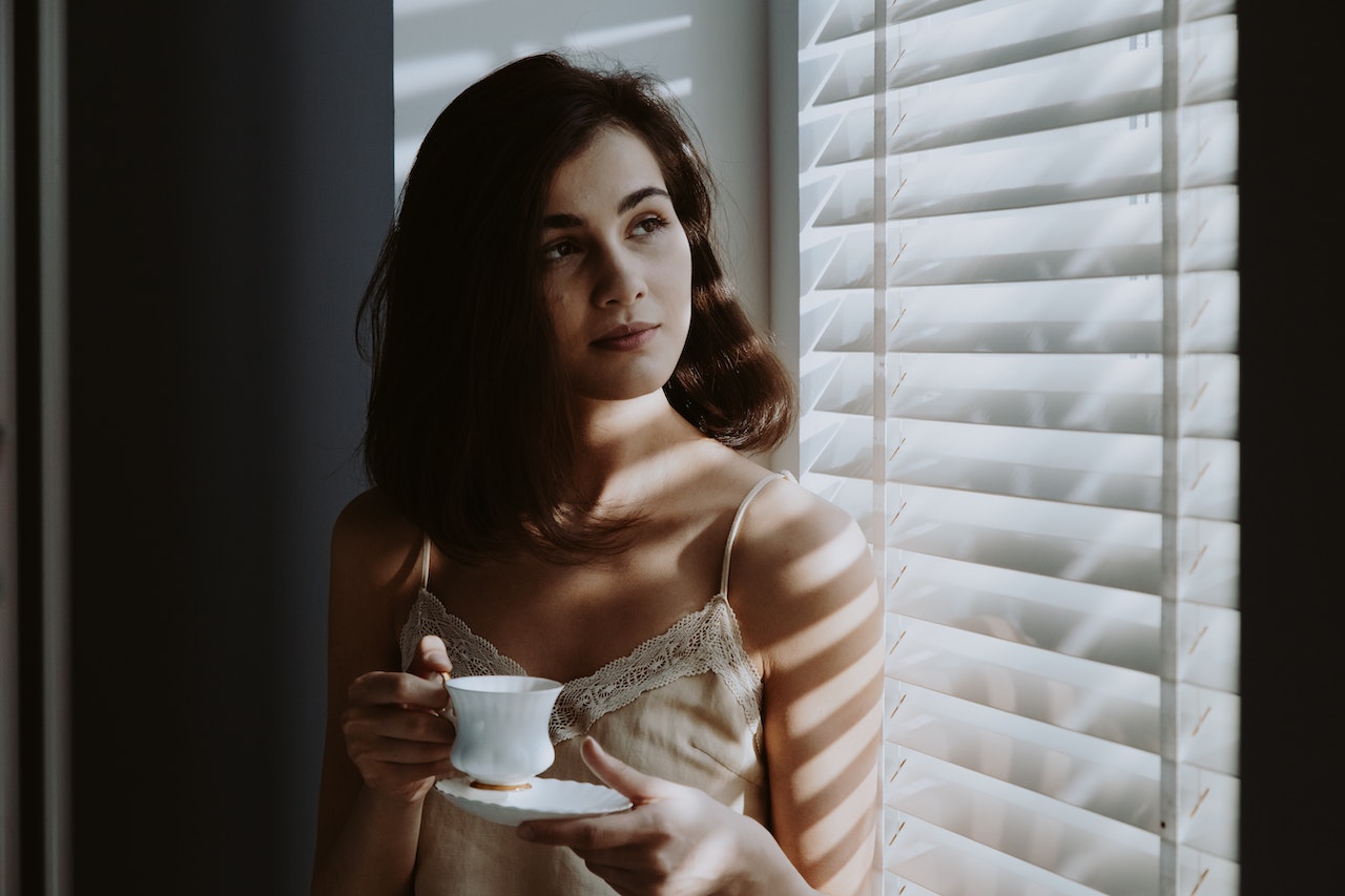 a woman drinking a cup of coffee in front of a window in the morning