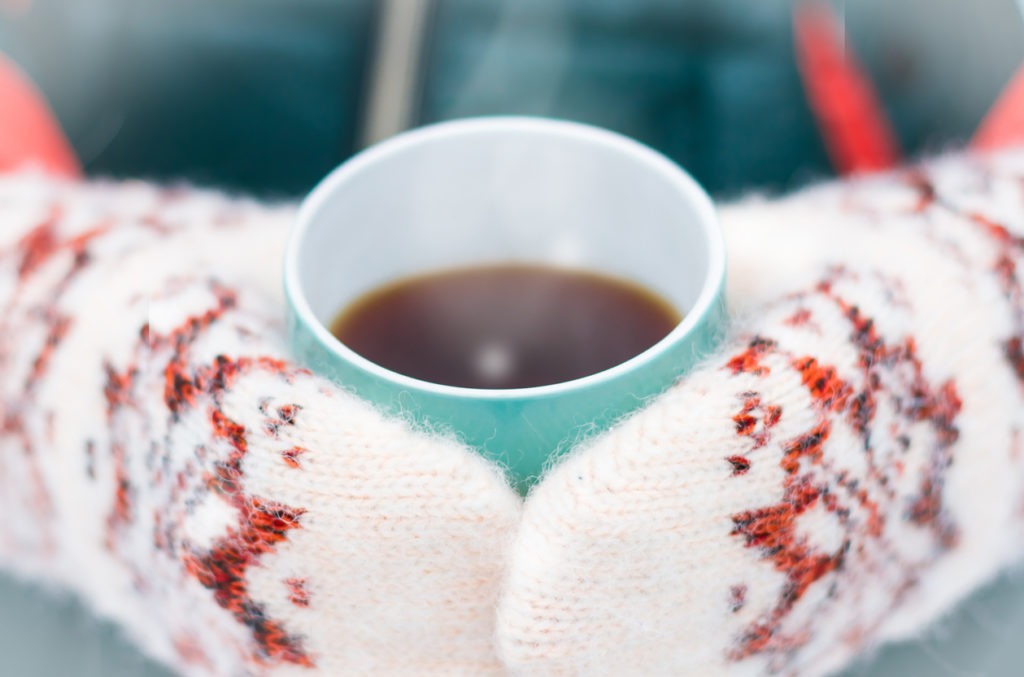 cup tea on woman's hand on mittens with ornament