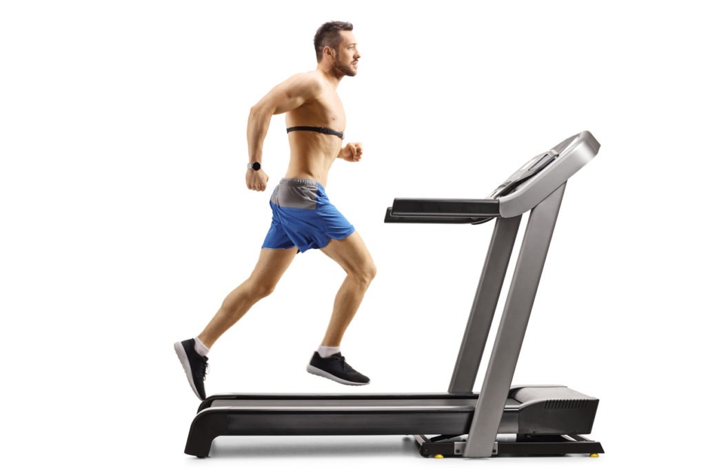 Young muscular man running on a treadmill and wearing a chest strap