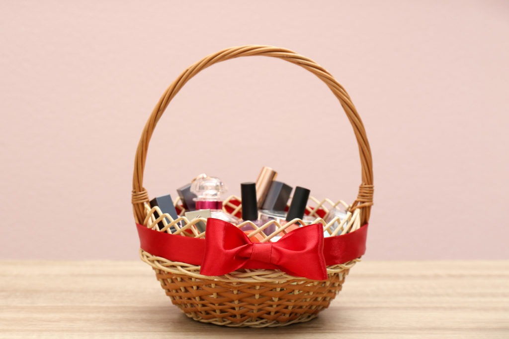 Wicker gift basket with cosmetic products on wooden table