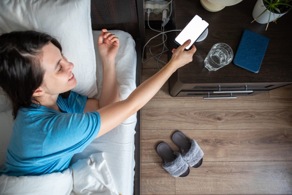 A woman taking a phone from a wireless charger from a bedside table.