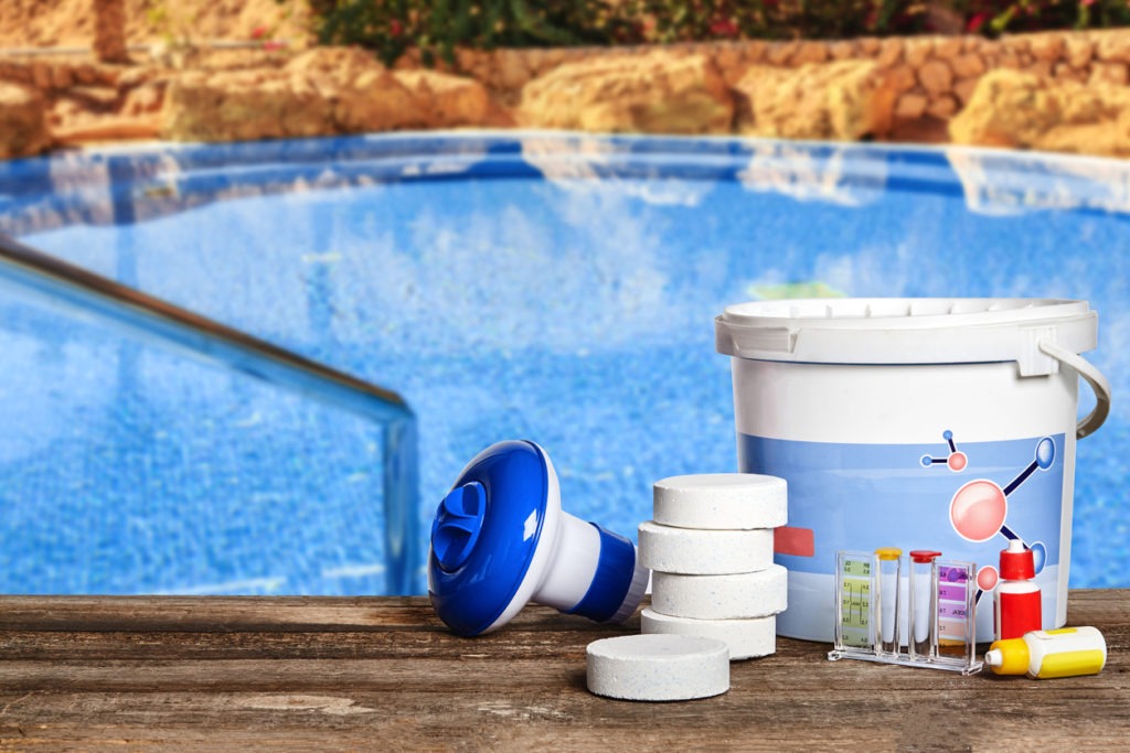 Superlative equipment with chemical cleaning products and tools for the maintenance of the swimming pool on a wooden surface against a green spaces background. Horizontal composition. Close-up front view
