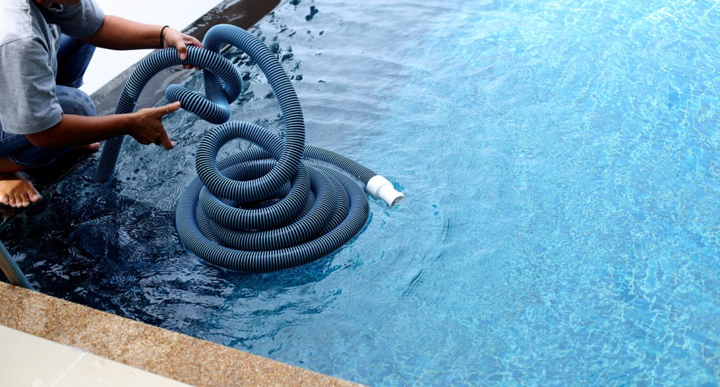 Woman Worker cleans private swimming pool with vacuum blue tube cleaner every week in Summer