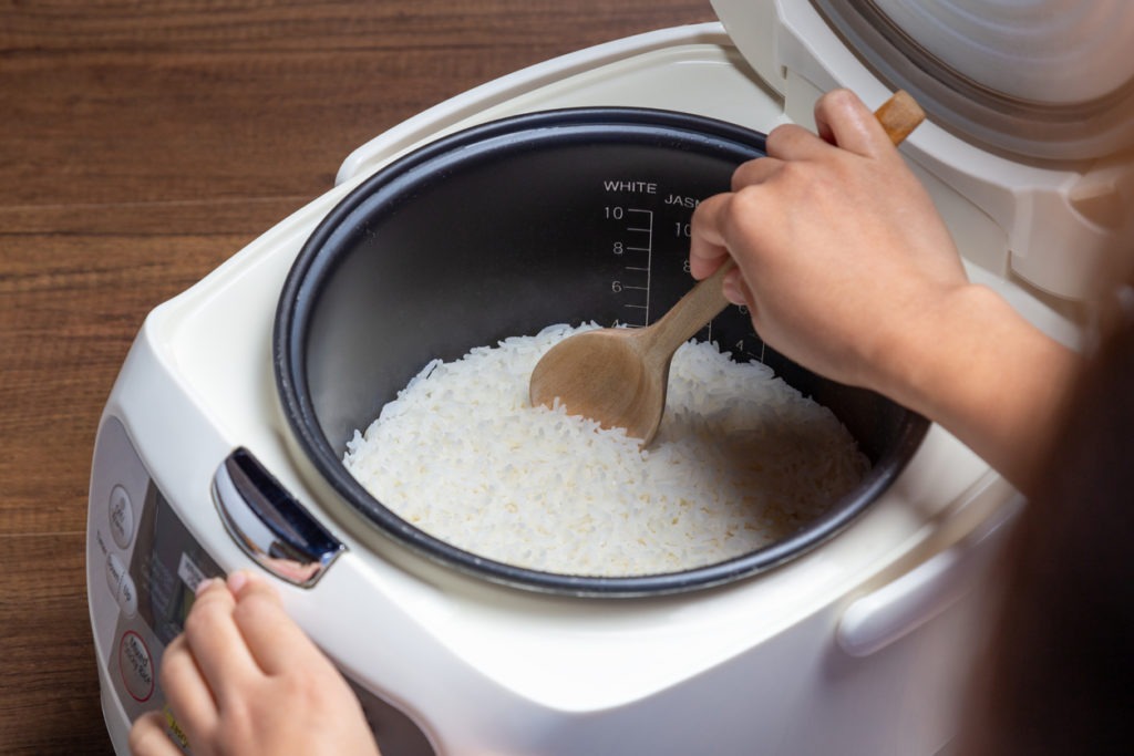 a woman’s hands scooping rice from a rice cooker