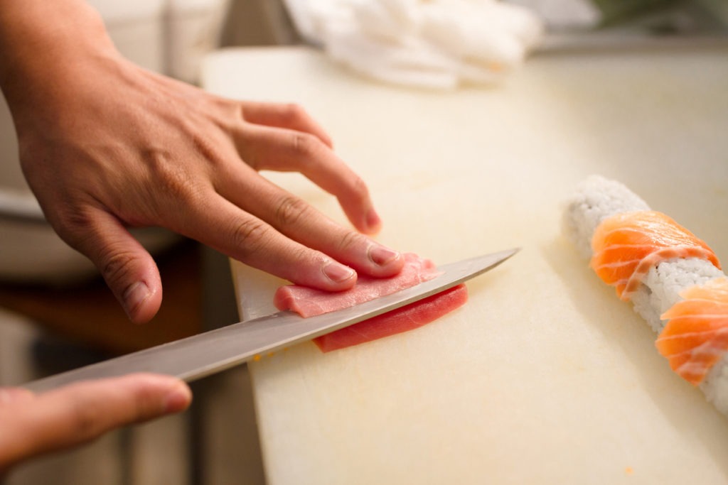 Photo close up on the hands of the Japanese sushi sashimi chef's knife, slicing the raw tuna fish for cooking maki sushi in the kitchen