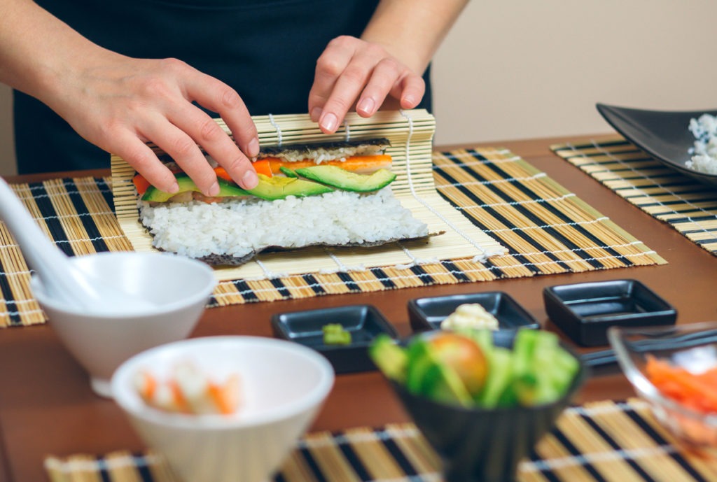 Detail of hands of woman chef rolling up japanese sushi