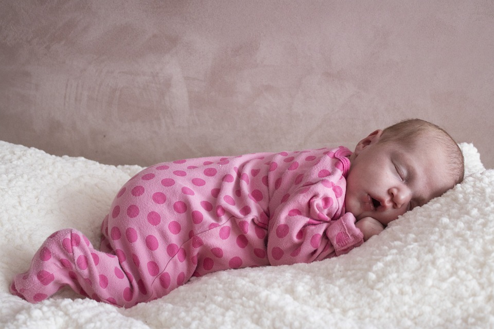 a-baby-in-a-pink-onesie-sleeping-in-a-white-bedding