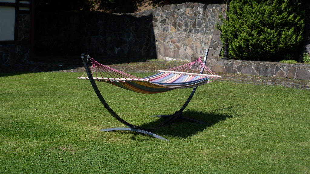 Colored hammock in the backyard. Fabric hammock on a metal stands in the garden. Striped fabric hammock with stand
