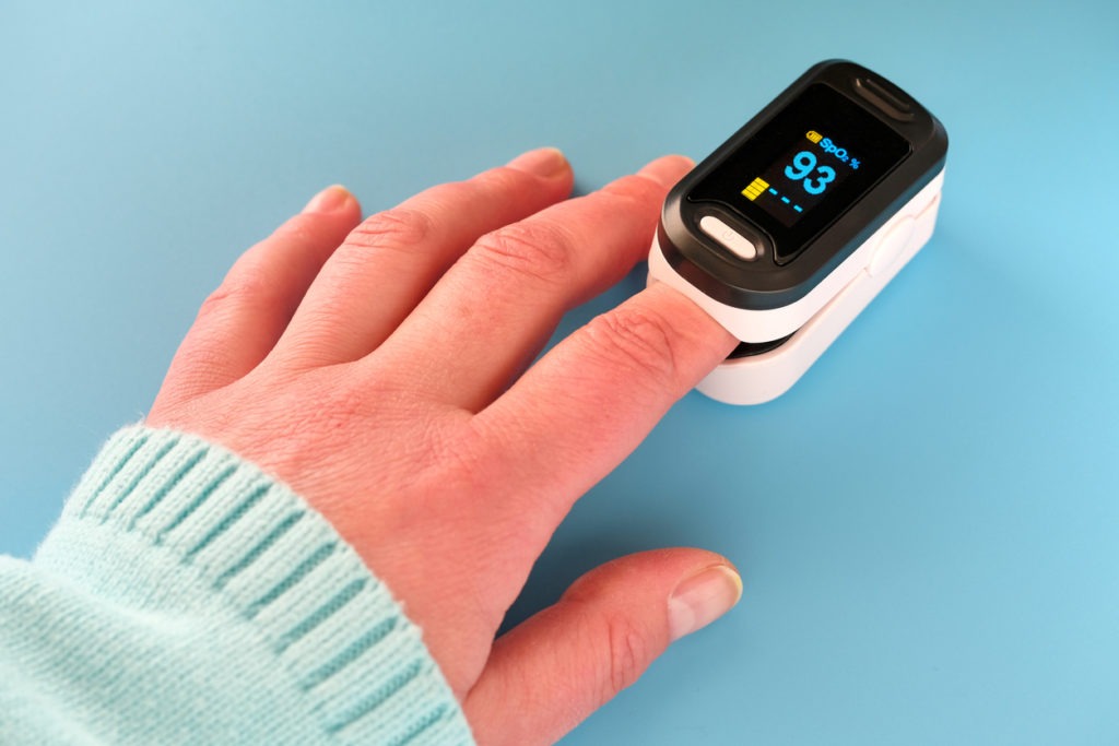Pulse Oximeter, finger digital device to measure person's oxygen saturation. Reduced oxygenation is an emergency sign of pneumonia, for instance caused by coronavirus. Device on Caucasian female hand.