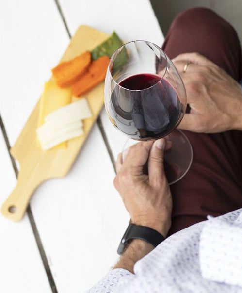 person holding a glass of wine by a cheese board