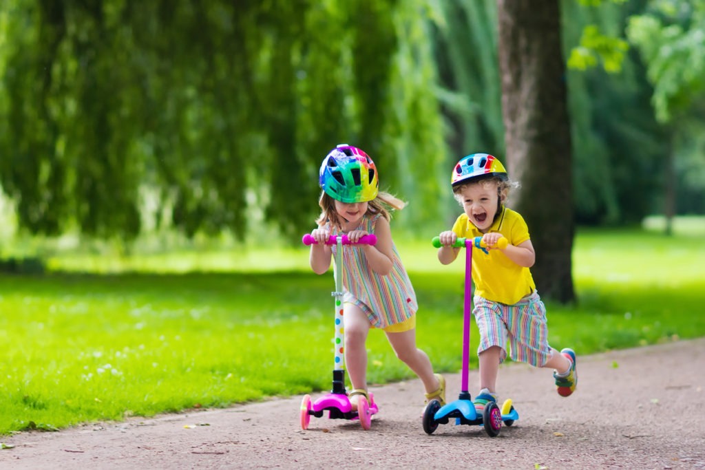 two kids riding on scooters outside