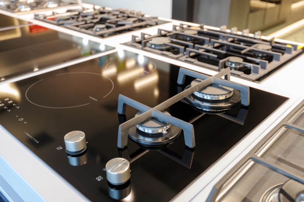 Hybrid gas and electric induction stove with black glass tray selling in appliance retail store showroom, closeup, selective focus