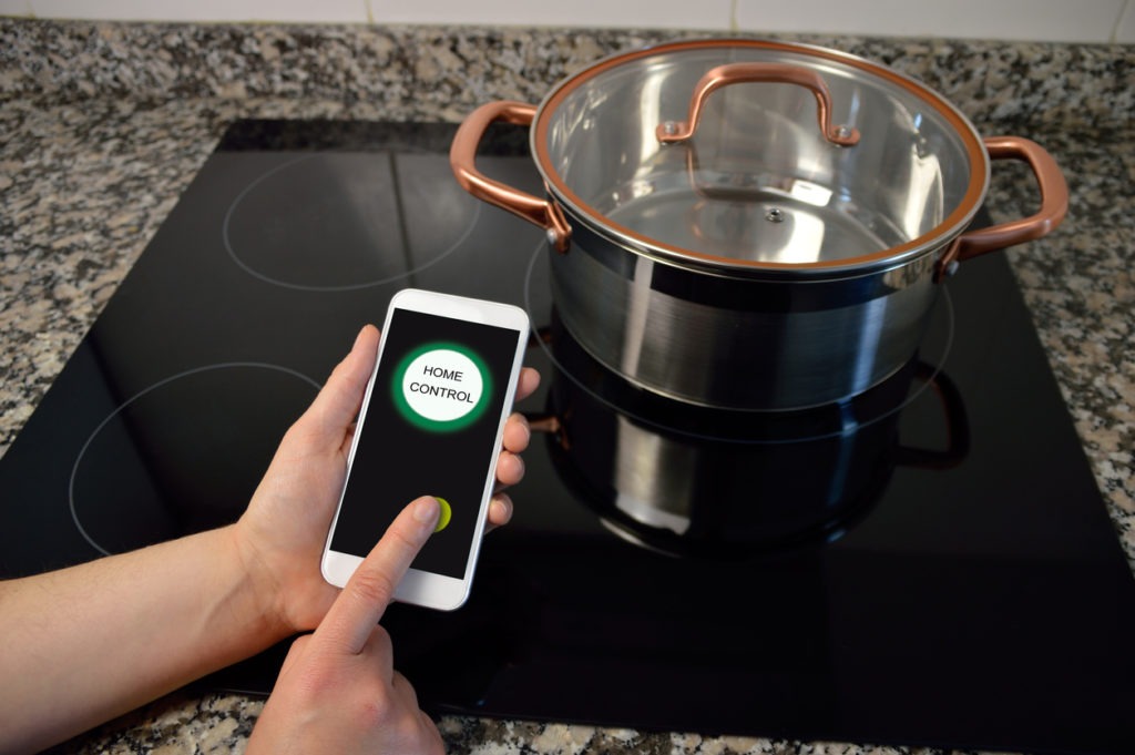 Man hand holding mobile phone smart control home cooker at kitchen