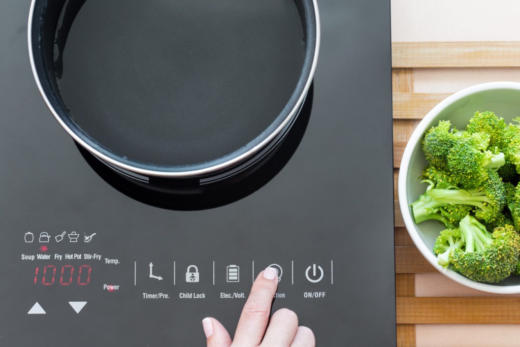 Woman selects function on Induction stove, cooking broccoli process