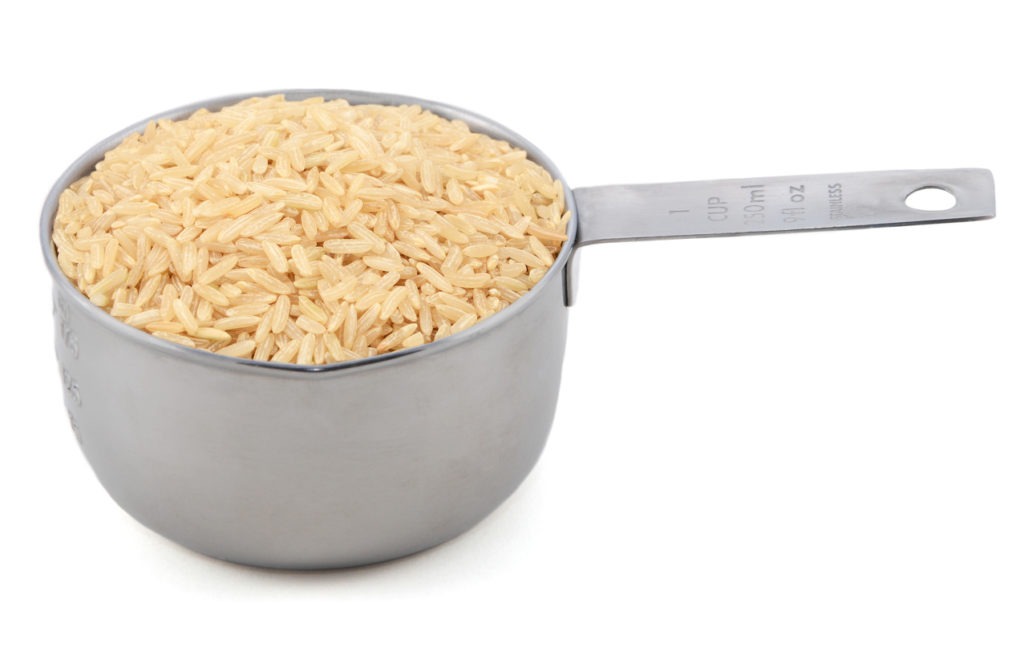 Long-grain brown rice in an American measuring cup, isolated on a white background