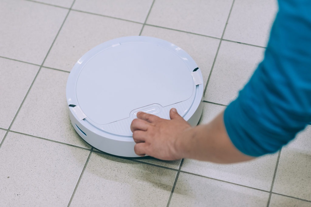 Man turns on a smart robot vacuum cleaner on a tile floor