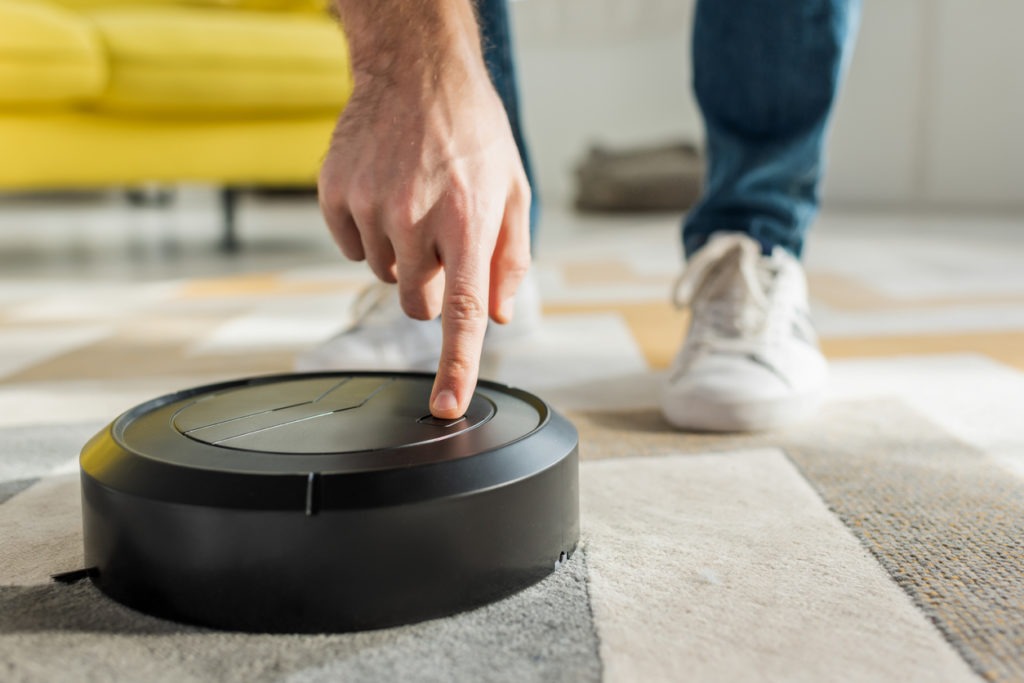 cropped view of man pointing with finger at robotic vacuum cleaner in living room
