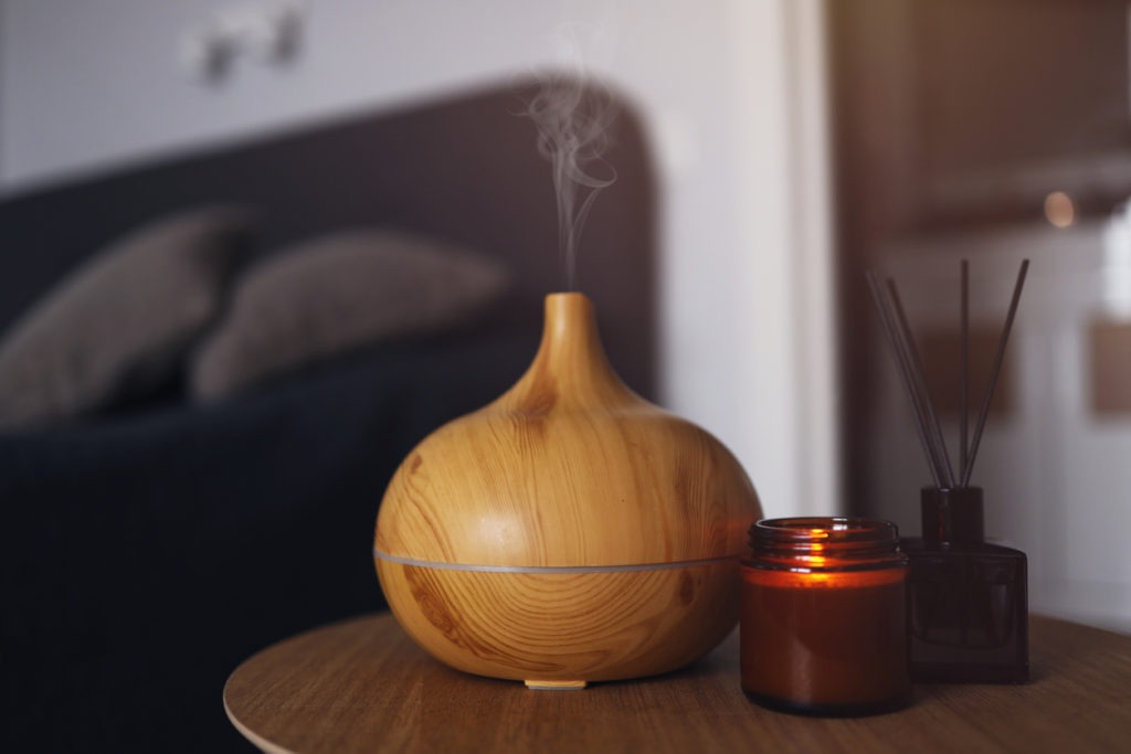 Aroma oil diffuser, air freshener and candle on a wooden table in the bedroom. Warm, atmospheric photography.