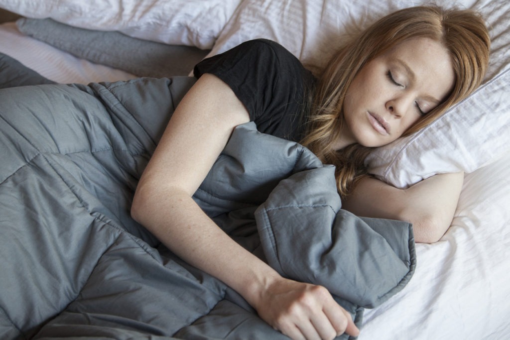 Young redhead woman using soft weighted blanket in her modern apartment