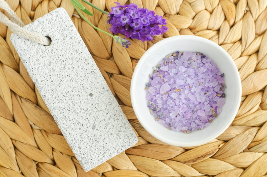 Small white bowl with purple lavender crystal bath salt (foot soak) and pumice stone. Homemade pedicure, spa and beauty treatment recipe.