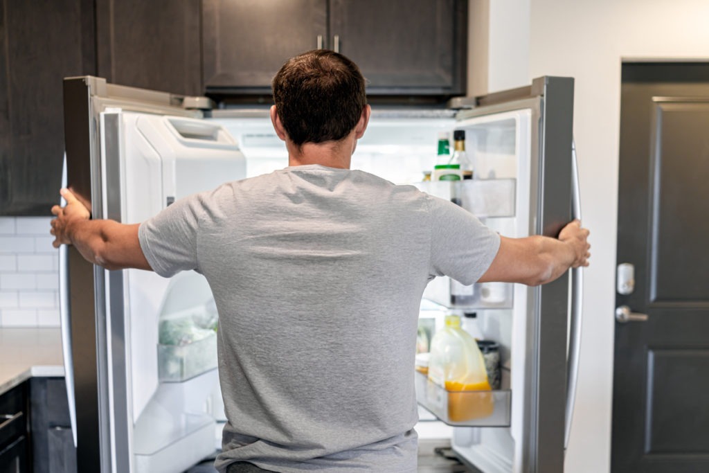 man opening fridge refrigerator doors domestic appliance searching for food inside with condiments and juice in modern kitchen