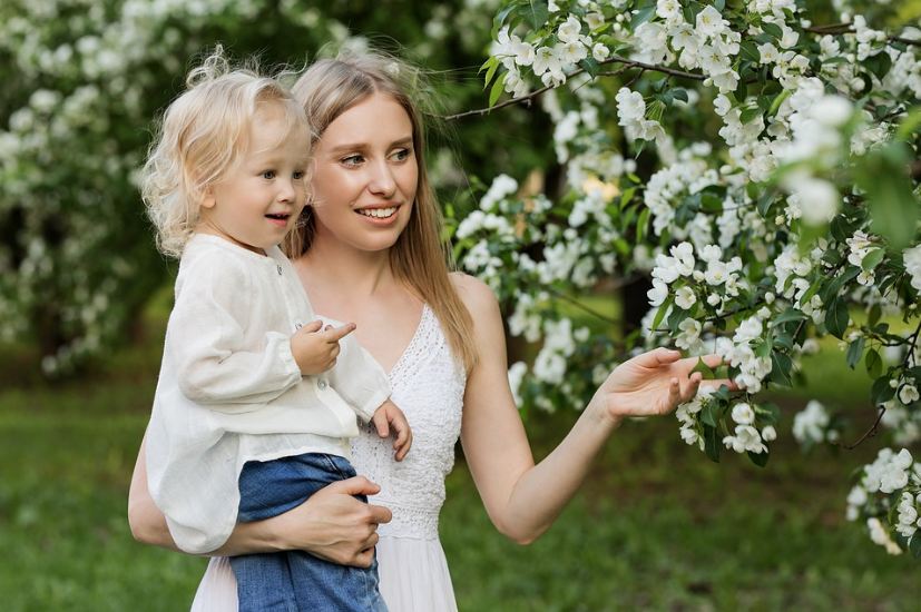 a mom carrying her daughter in a garden, flowers, trees, garden