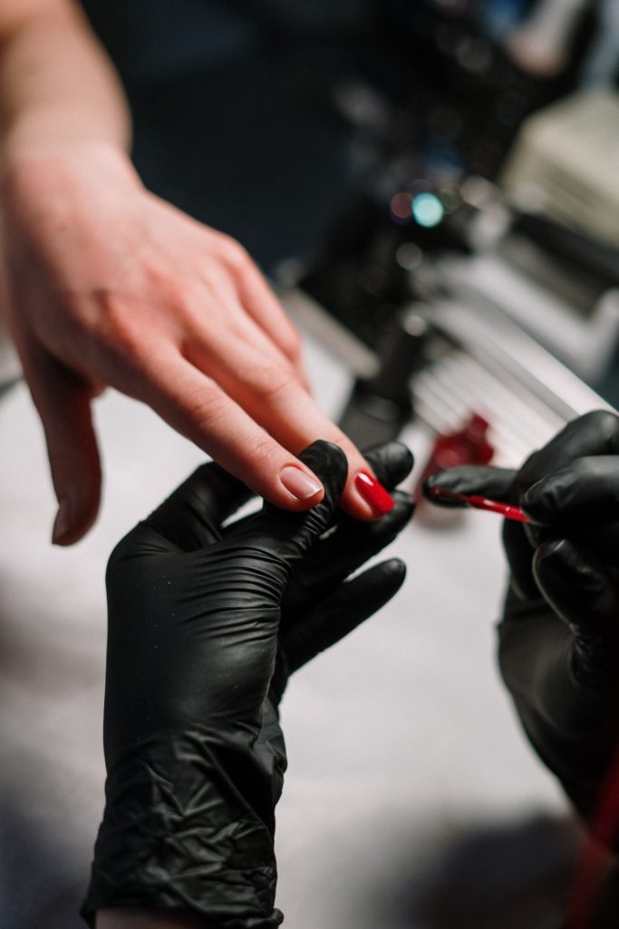 person-in-black-leather-gloves-holding-red-nail-polish
