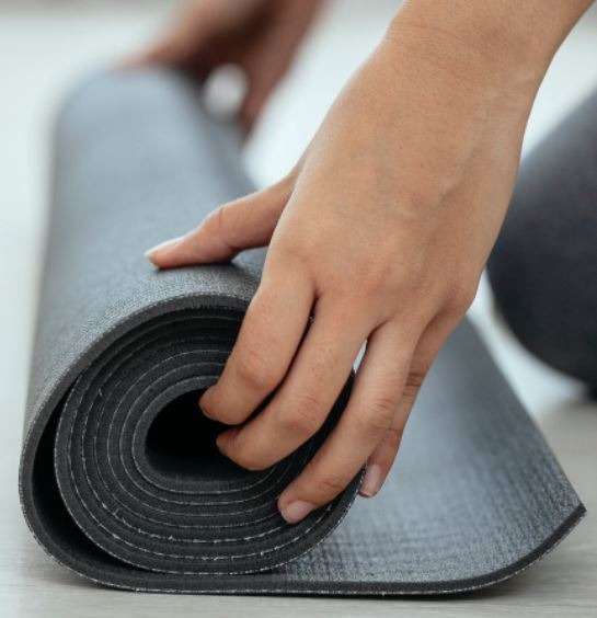 crop-female-holding-rolled-mat-on-floor