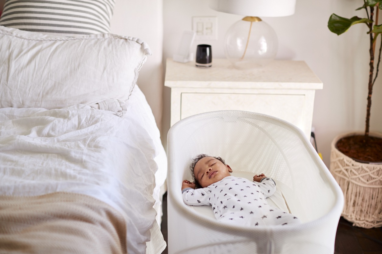 A baby sleeping in a bassinet next to his parents’ bed