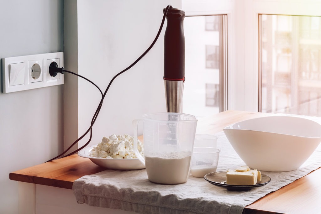 A corded immersion blender plugged in and placed in a bowl with ingredients