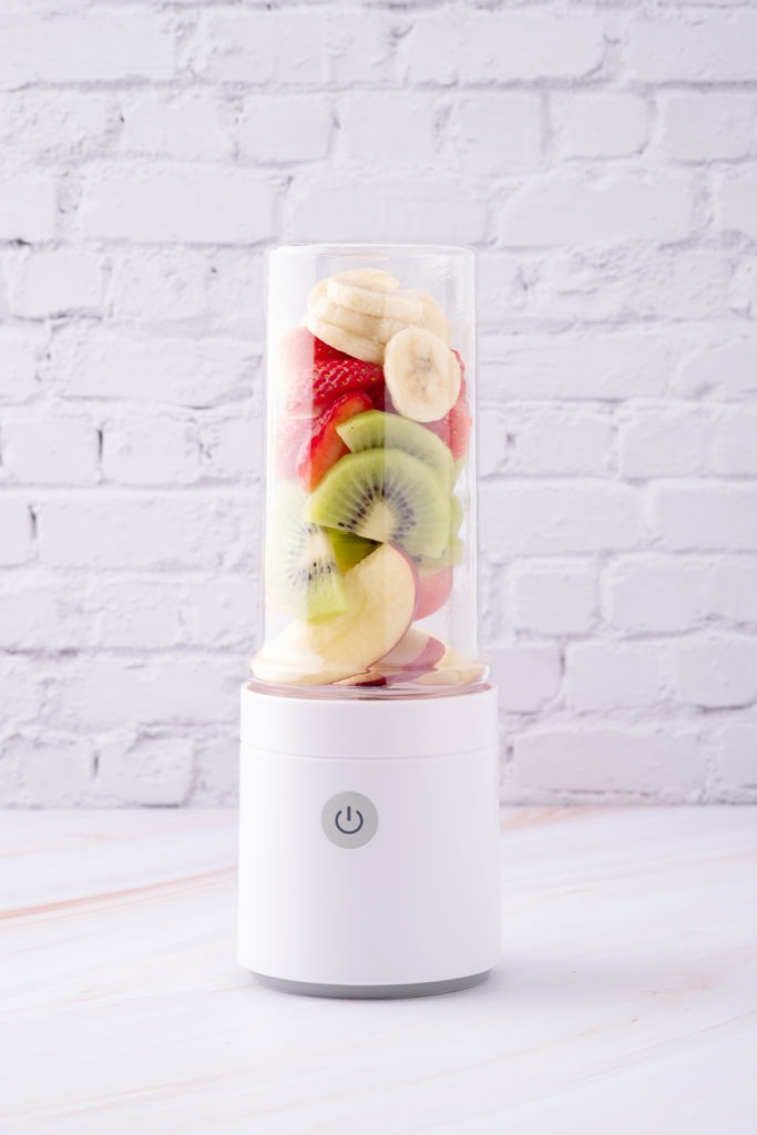 A portable blender with apples, bananas, kiwis, and strawberry inside