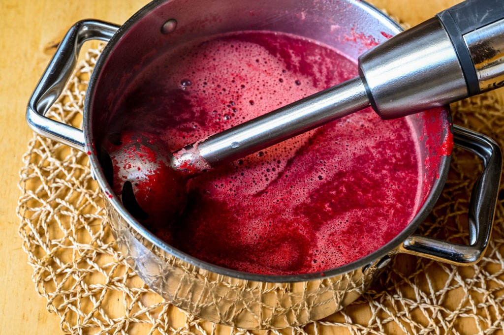 An immersion blender in pot with beetroot soup