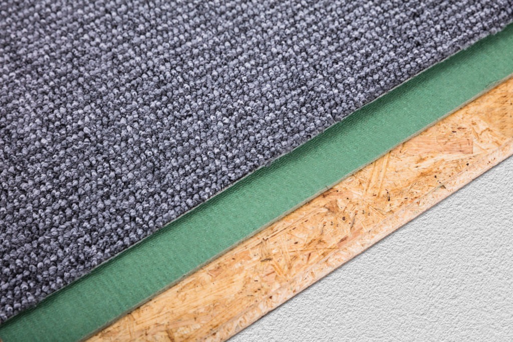 Close-up-of-a-grey-carpet-with-a-green-rug-pad-underneath