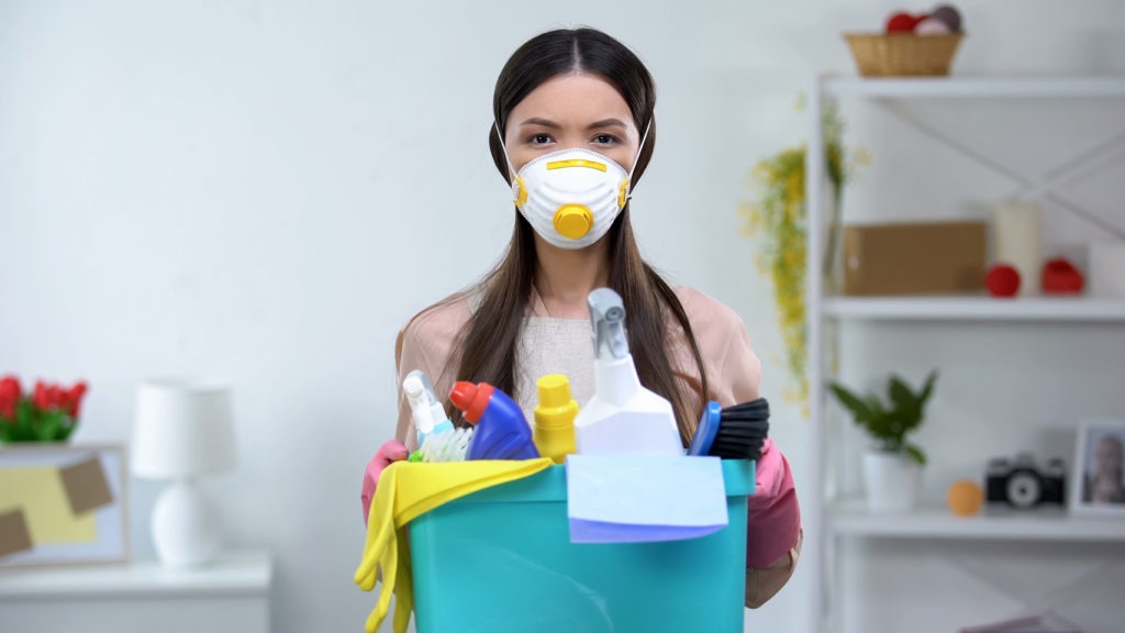 Female in respirator holding a basket of household chemicals