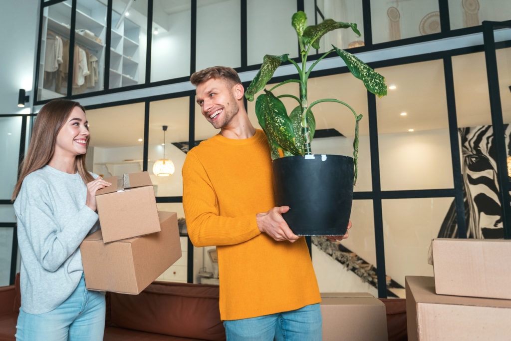 Man holding a plant while moving into a new house with his girlfriend