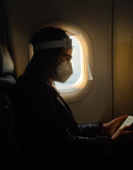 Man-with-facemask-reading-book-in-an-airplane-window-seat