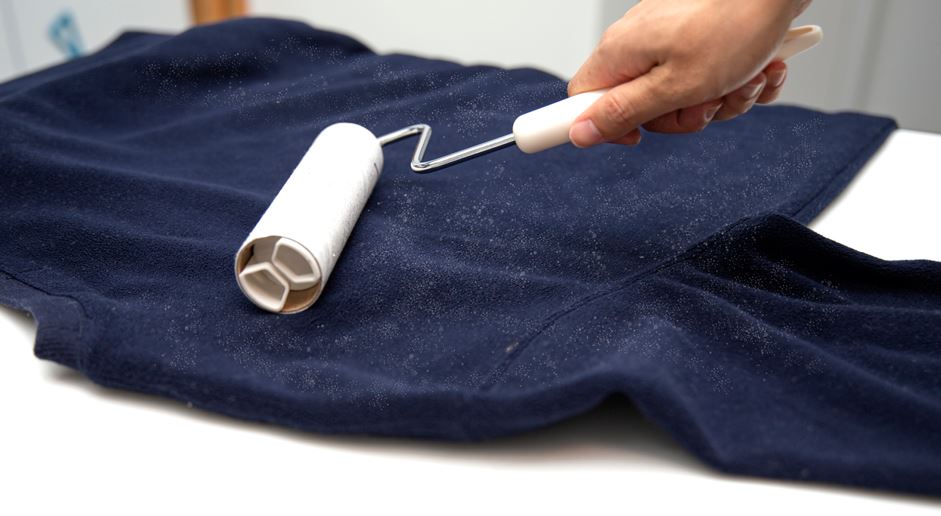 Using lint roller to remove pieces of hair and debris from clothes