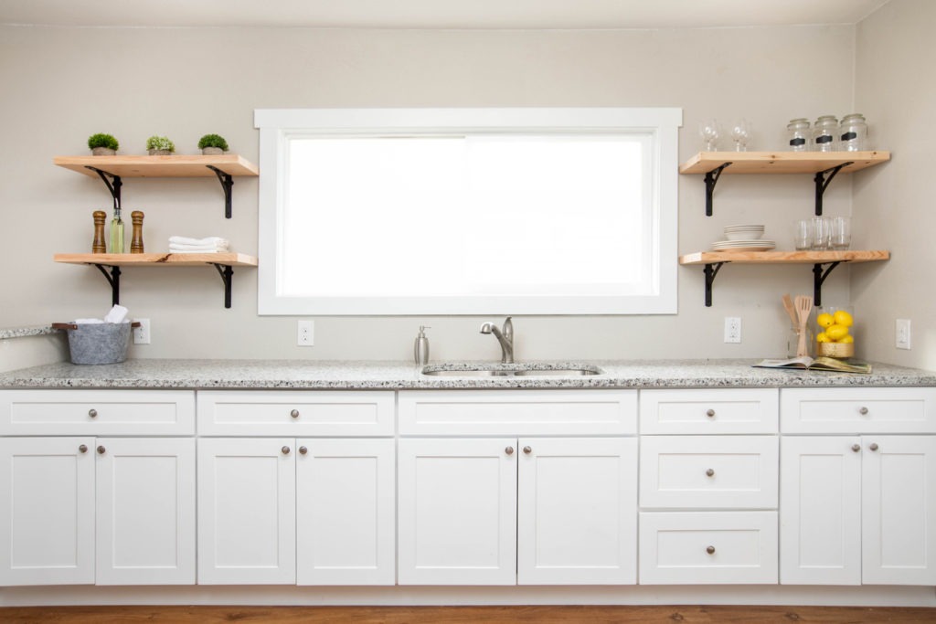 White kitchen cabinets with a granite countertop and wooden floating shelves