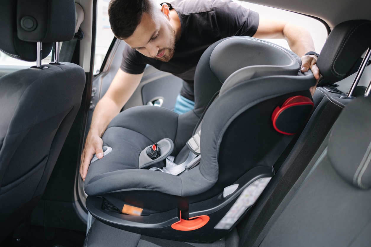 a father installing a car seat at the car’s back seat