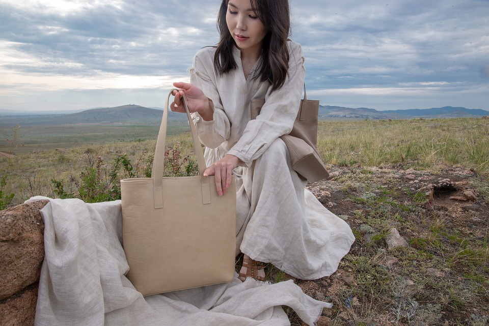 a woman in a beige dress carrying one brown bag on her shoulder and holding another beige bag
