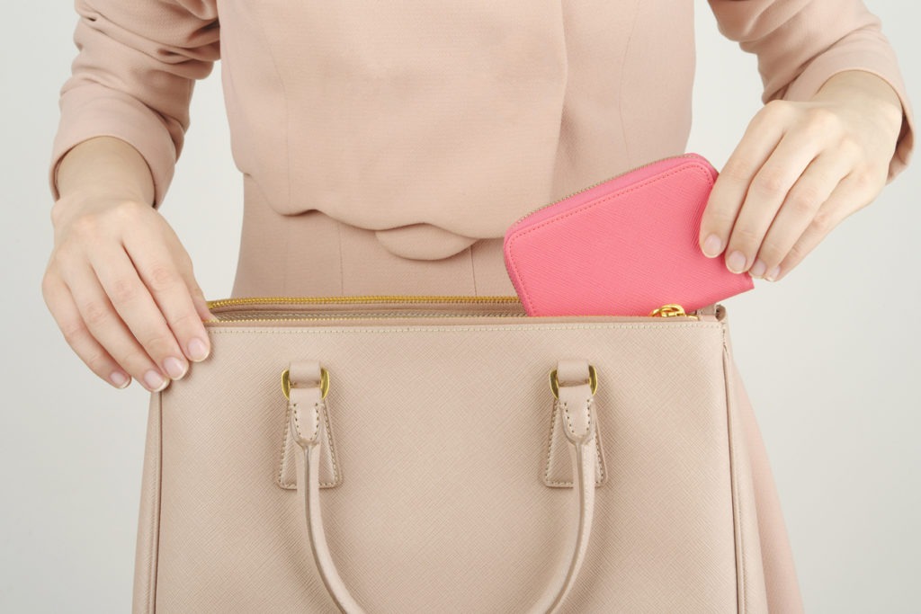 a woman putting her wallet inside her beige handbag