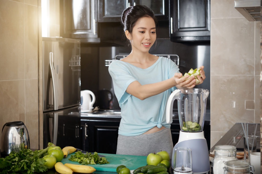 Asian woman putting fruits in blender