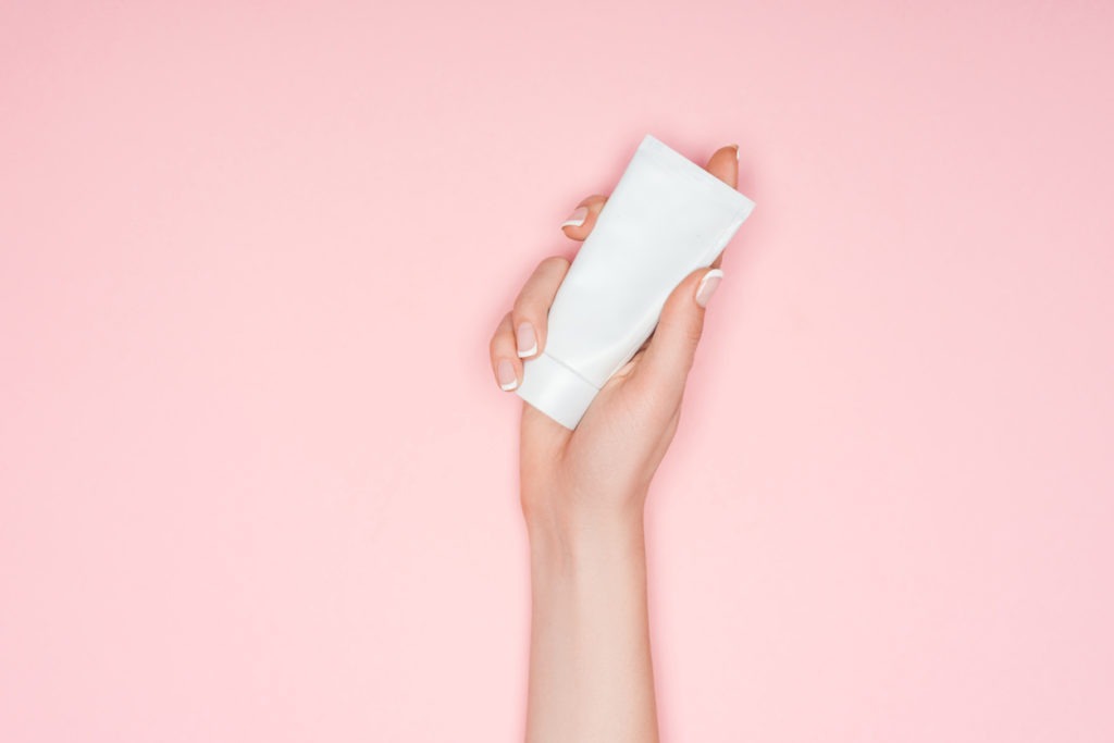 cropped view of woman holding hand cream isolated on pink with copy space