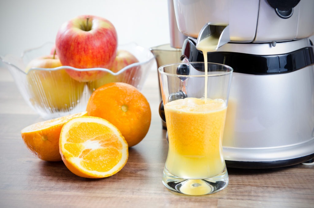 Juicer and orange juice. Fruits in background
