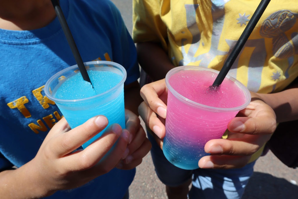 Kid's hands holding colorful granita, fruit slush drinks in summer