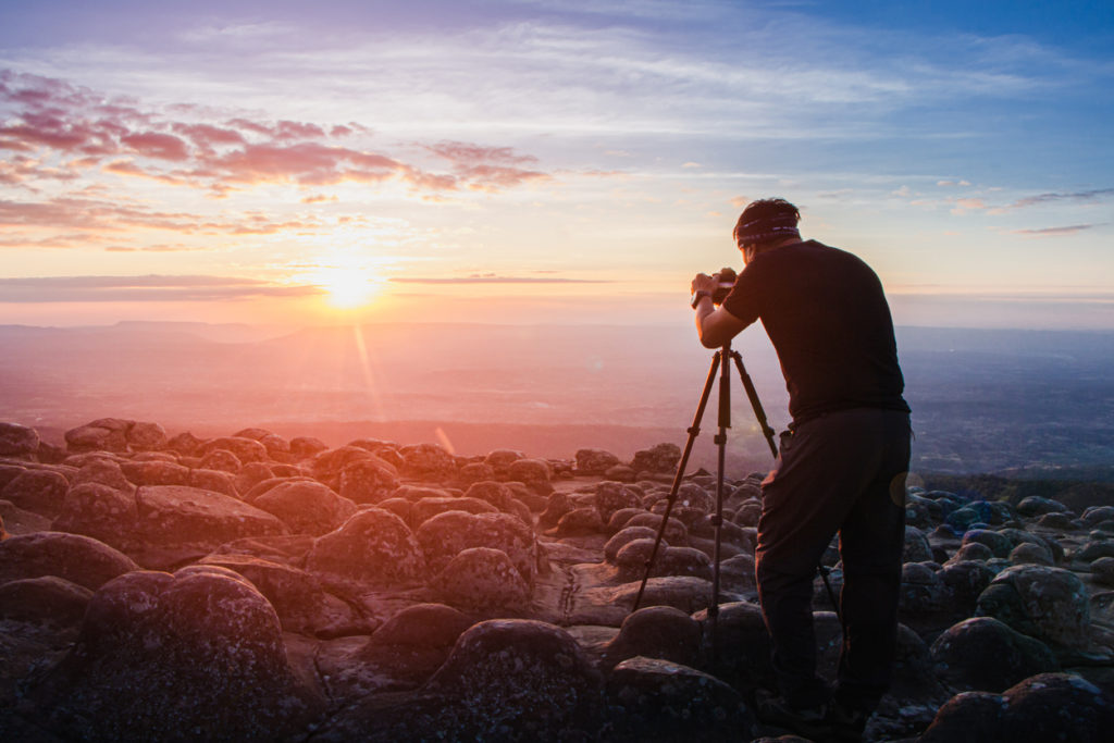 man photographer holding a camera to shoot nature sunrise at mountain scenery.Tourists take pictures of sunset nature with camera on a tripod 