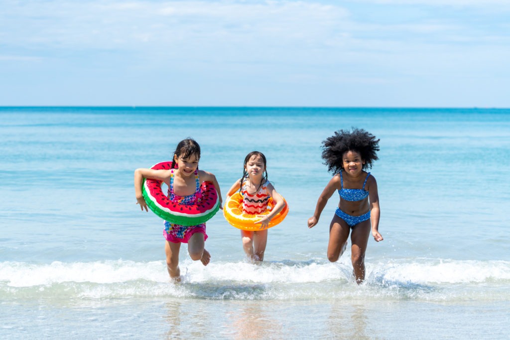 Little African and Asian girl playing in sea water together at tropical beach on summer vacation
