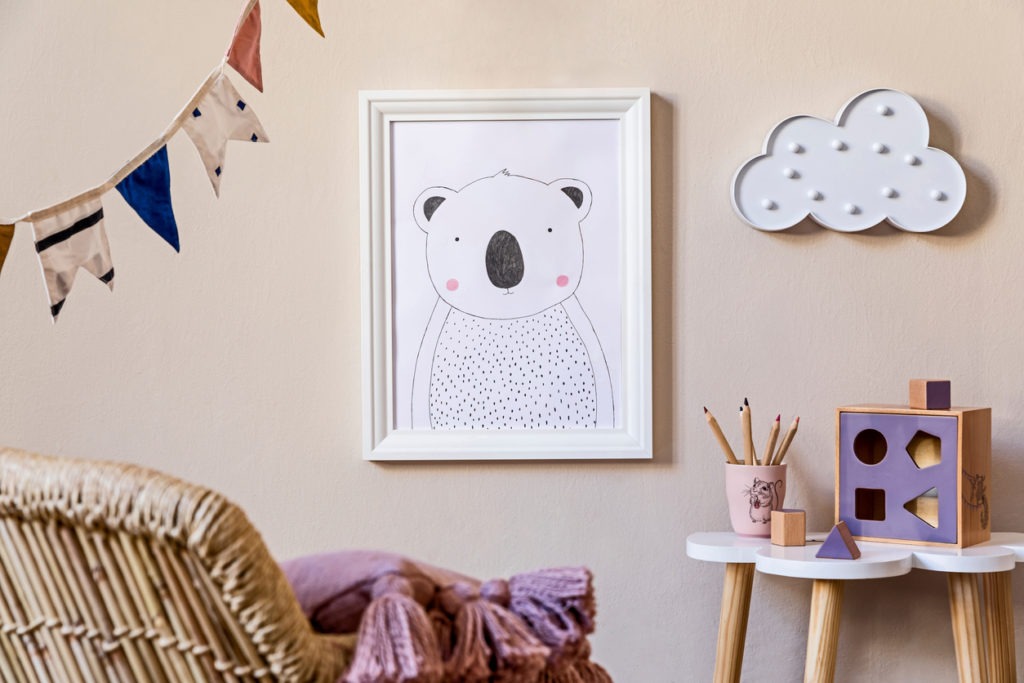 Stylish scandinavian nursery interior with mock up photo frame, wooden toys, design furniture, pillows and accessories. Beautiful decoration on the beige background wall. Home decor for children room