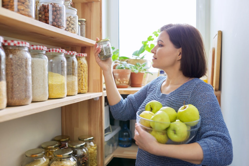 Woman with bowl of green apples in pantry, organizing in kitchen