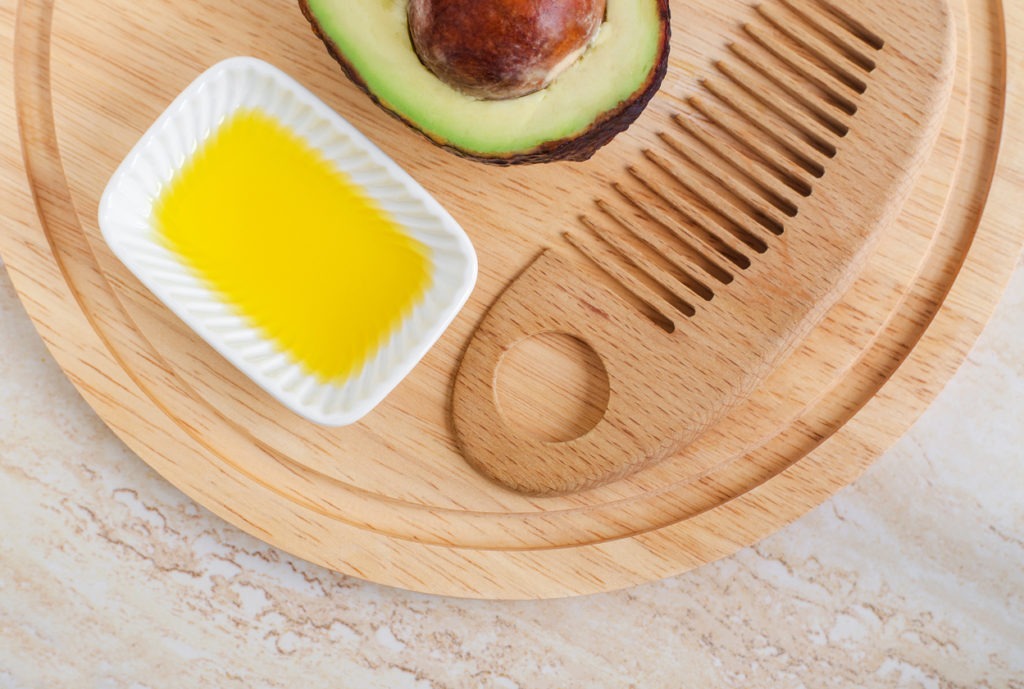 A little white bowl of fresh avocado oil and a wooden hairbrush. 